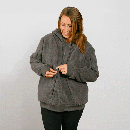 Woman wearing a charcoal gray sherpa zip hoodie with hood over her head, looking down.
