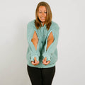 Woman wearing a seafoam color zip hoodie with cutout sleeves, smiling while looking down.