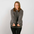 Woman wearing a gray sherpa zip hoodie with sherpa lining over a dark shirt, smiling with hands in pockets.