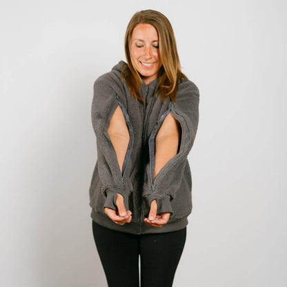 Woman wearing a gray sherpa zip hoodie with open sleeves, smiling while looking downward.