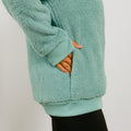 Seafoam colored sherpa hoodie with thumb holes and open hand access cutouts showing hand in side pocket.