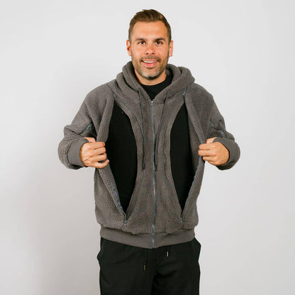 Man wearing gray sherpa zip hoodie over black shirt, holding jacket open against white background.