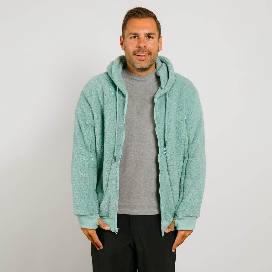 Man wearing seafoam color sherpa zip hoodie over gray t-shirt and black pants against white background.