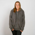 Woman wearing a gray sherpa zip hoodie with hood and black pants, smiling at camera.