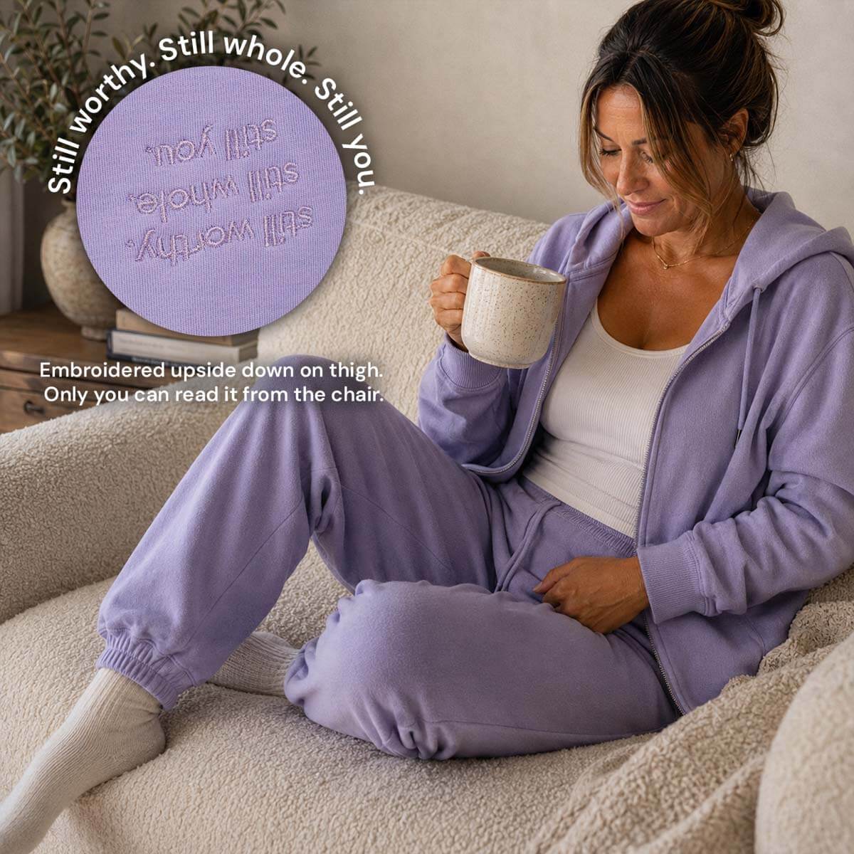 Woman sitting on cream couch in a comfy, warm atmosphere/living room wearing comfy lavender sweatsuit sipping her morning coffee.