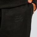 Black sweatpants with embroidered text on the leg, worn with a dark sweater and orange-toned shoes.