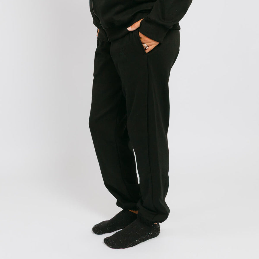 Black sweatpants with ripped thigh cutouts worn with black socks against a white background.