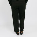 Person wearing black sweatpants standing against white background, viewed from behind.