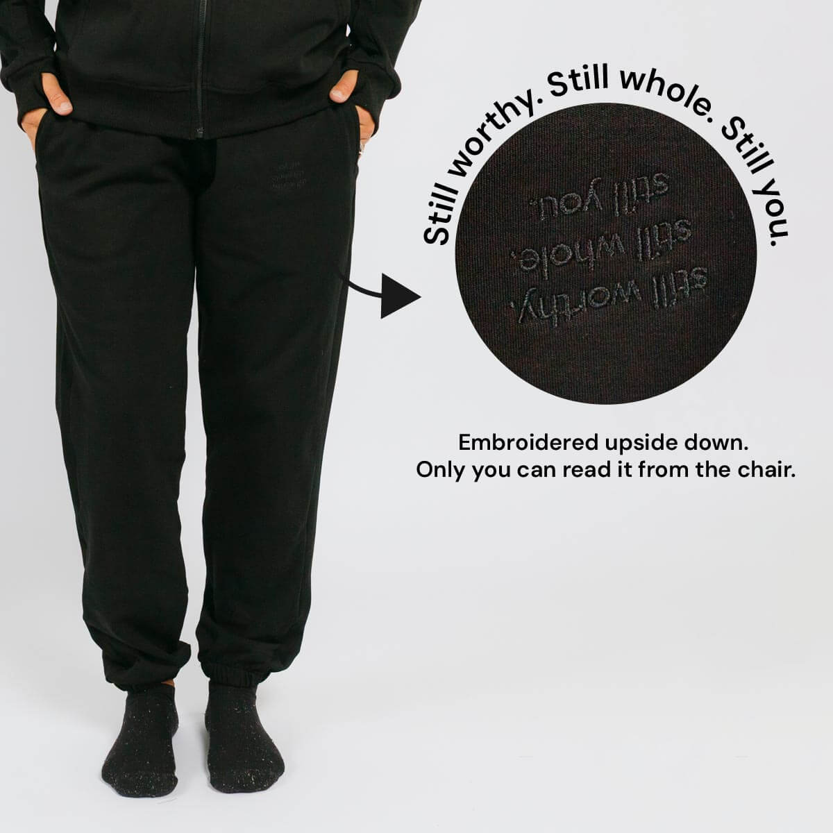 Black sweatpants with embroidered text on the back pocket that reads upside down when worn.