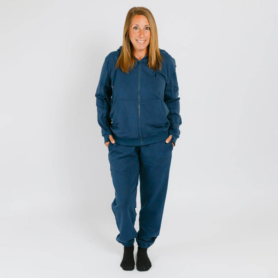 Woman wearing a navy blue zip-up hoodie and matching sweatpants with black socks.