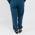 Rear view of person wearing navy blue sweatpants and dark socks against white background.
