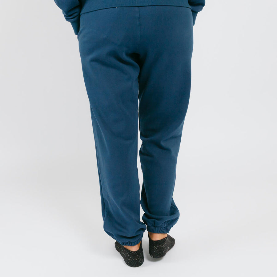 Rear view of person wearing navy blue sweatpants and dark socks against white background.