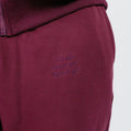 Burgundy sweatpants with ribbed waistband and embroidered text detail on the thigh.