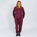 Woman wearing a burgundy zip-up hoodie and matching sweatpants, standing against a white background. | Model is 5'3" 130lbs wearing size S