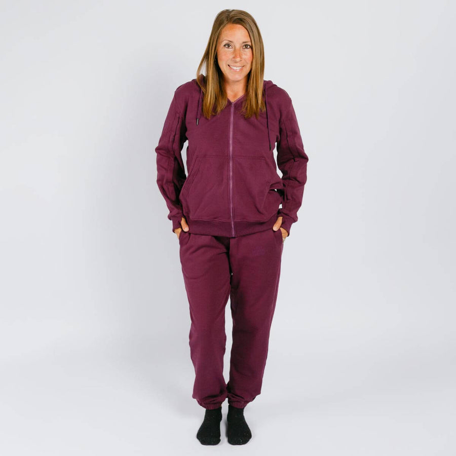 Woman wearing a burgundy zip-up hoodie and matching sweatpants, standing against a white background.