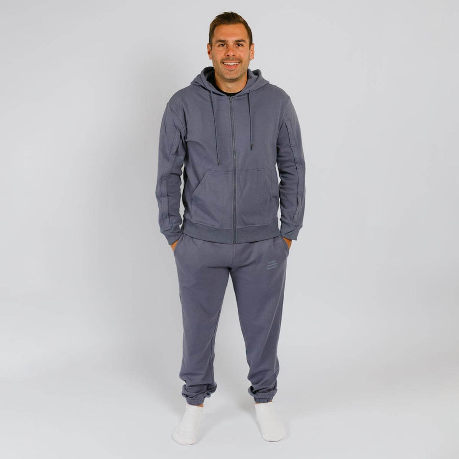 Man wearing a slate blue zip-up hoodie and matching gray sweatpants with white socks.