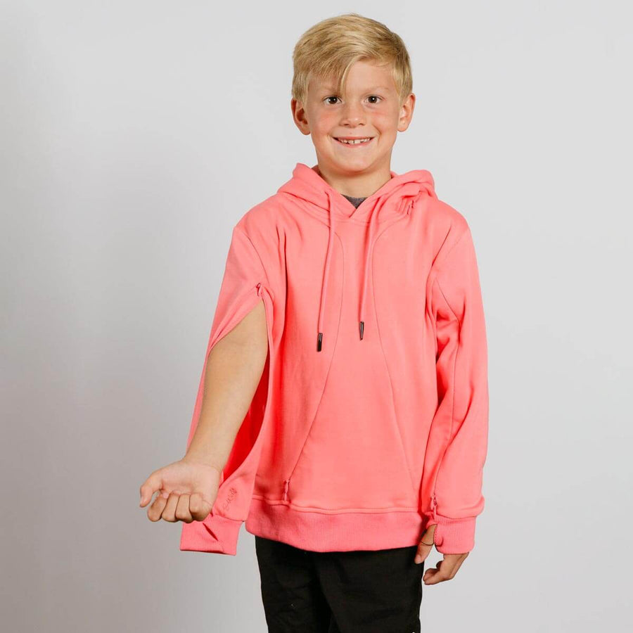 Young boy with blonde hair smiling while wearing a bright coral pink hoodie and black pants.