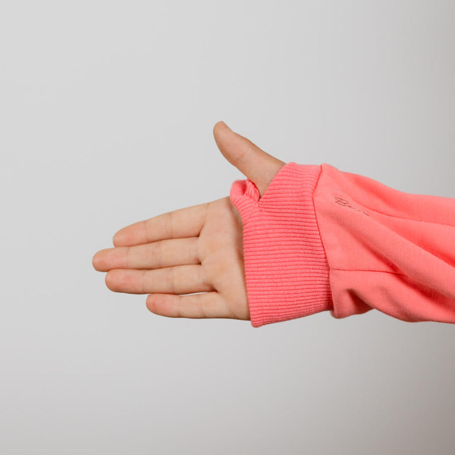 Child's hand extended from coral-pink ribbed sleeve cuff against neutral background.